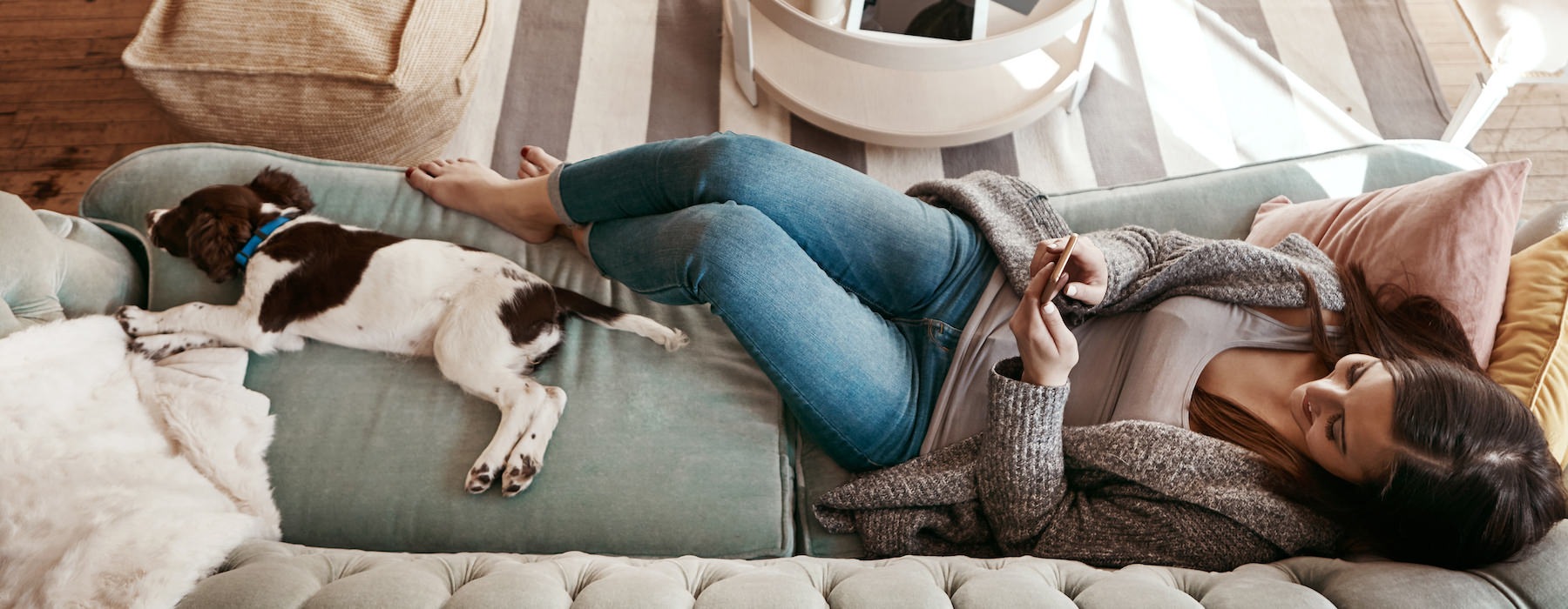 woman laying on a couch on her phone with her dog
